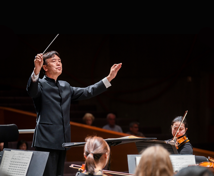 A conductor stands with arms outstretched, his baton in the air.